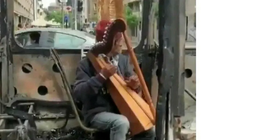 Gjør det beste ut av situasjonen. En mann spiller harpe i en nedbrent buss i Santiago de Chile.