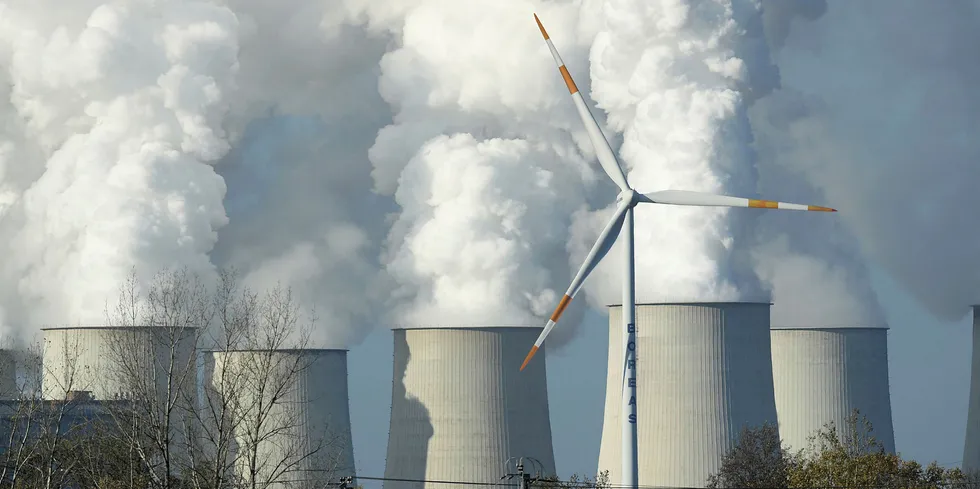 A wind turbine spins as steam rises from the cooling towers of the Jaenschwalde coal-fired power plant near Peitz, Germany.