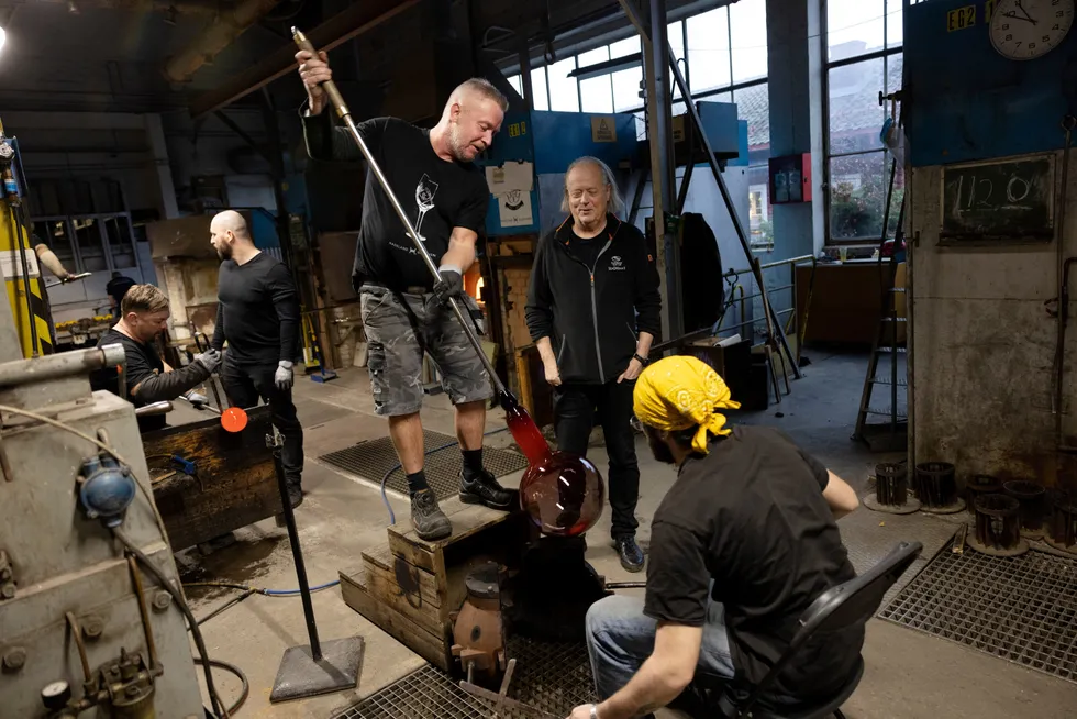 – Her har folk jobbet i 30 og 40 år, sier eier i Hadeland Glassverk Atle Brynestad i midten mens Frode Østby blåser i det som skal bli en lampe og Stylianos Hansen Nicolou holder formen.