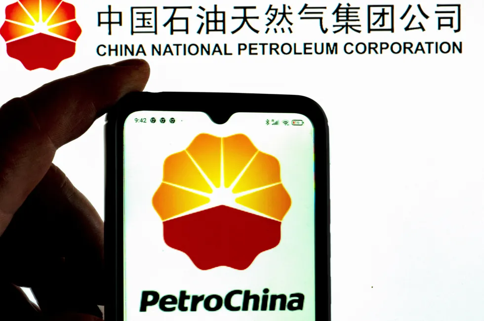 A person holds a smartphone displaying the PetroChina logo in front of a sign for its parent company, CNPC.