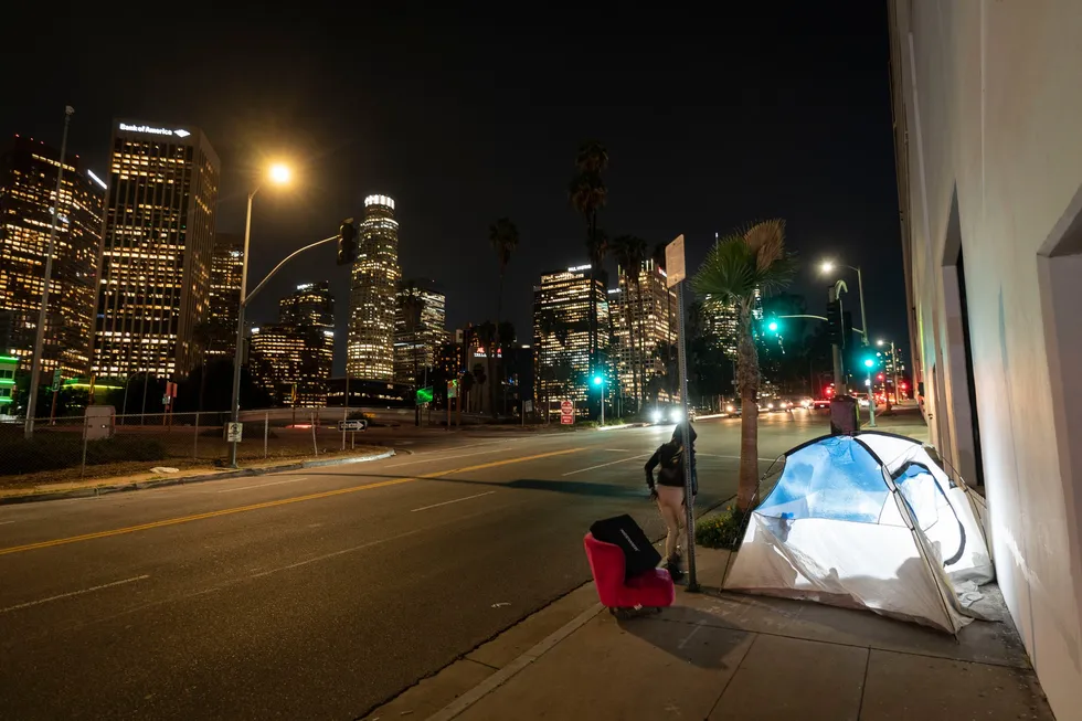 En kvinne går forbi en hjemløs persons telt med en stol i Los Angeles. En studie fra University of California, San Francisco viser at hjemløse i California kjempet med dårlig helse og dyp fattigdom før de ble hjemløse.