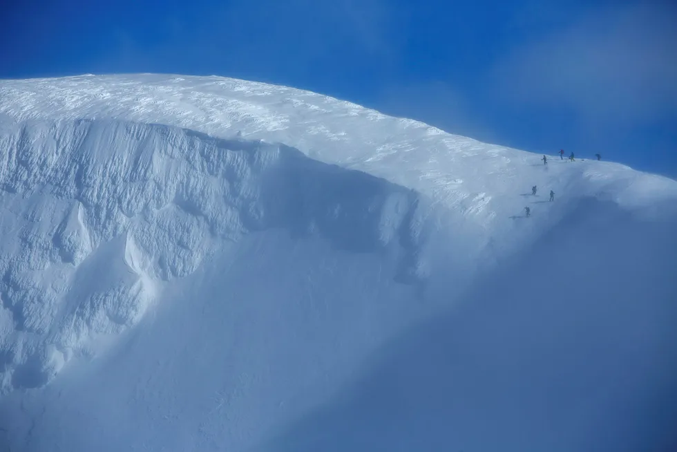 En gruppe skikjørere lister seg forsiktig inn i Mørkholla gjennom den trange inngangspassasjen mens det blåser hardt fra sørøst. Foto: Thomas T. Kleiven