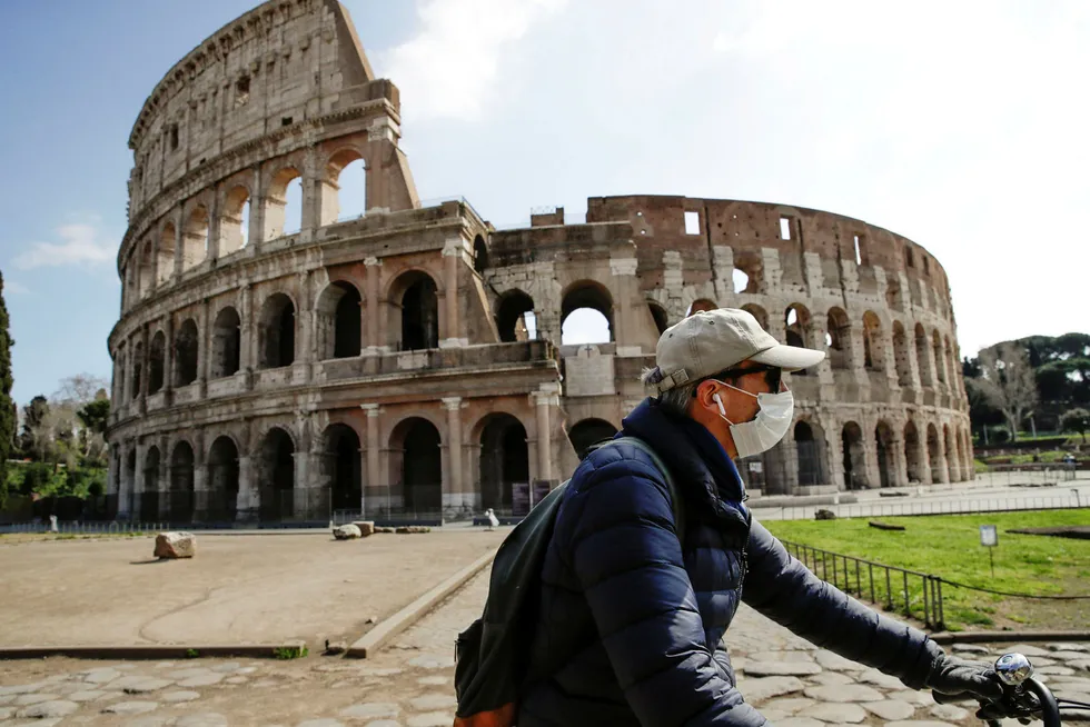 Italia letter på restriksjonene. Her sykler en mann med ansiktsmaske forbi Colosseum i Roma.