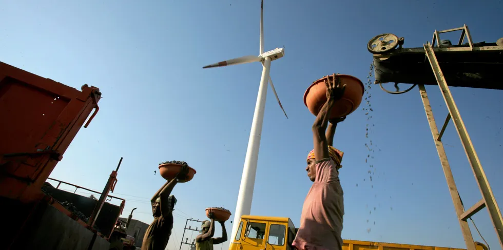 A laborer is seen working at a deisel powered crusher infont of a wind turbine. . India wind.