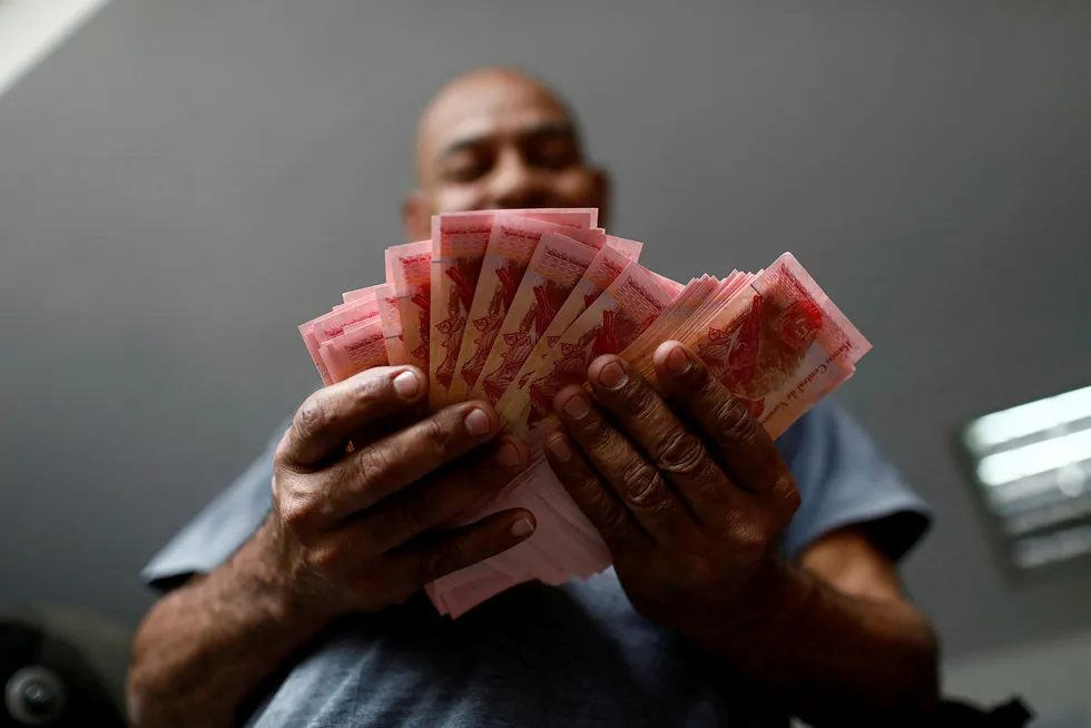 Venezuela sliter med enorm inflasjon. Nå fjernes flere nuller på pengesedlene. På bildet teller en tjenestemann penger på en parkeringsplass i Caracas i mai. Foto: Marco Bello/Reuters/NTB Scanpix