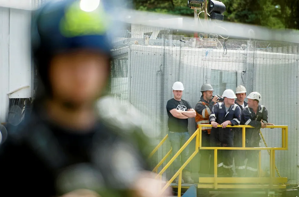 Site crew members look on as police officers in body armour line the perimeter fence of the test drill site operated by British energy firm Cuadrilla Resources