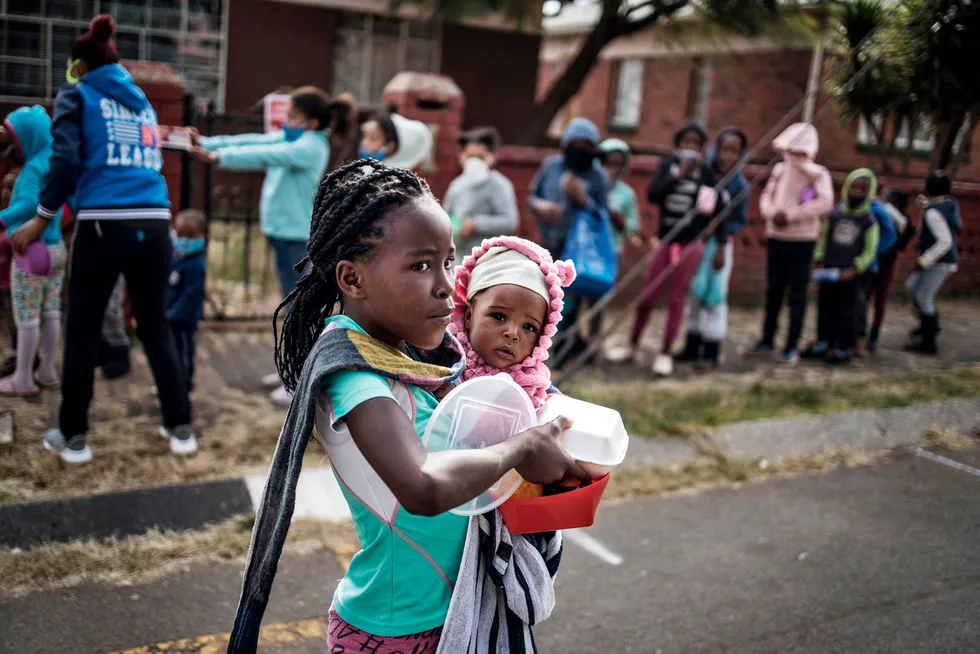 Et barn bærende på et søsken har fått utdelt mat av en grasrotorganisasjon i Johannesburg i Sør-Afrika. Fattige rammes hardt av koronapandemien.