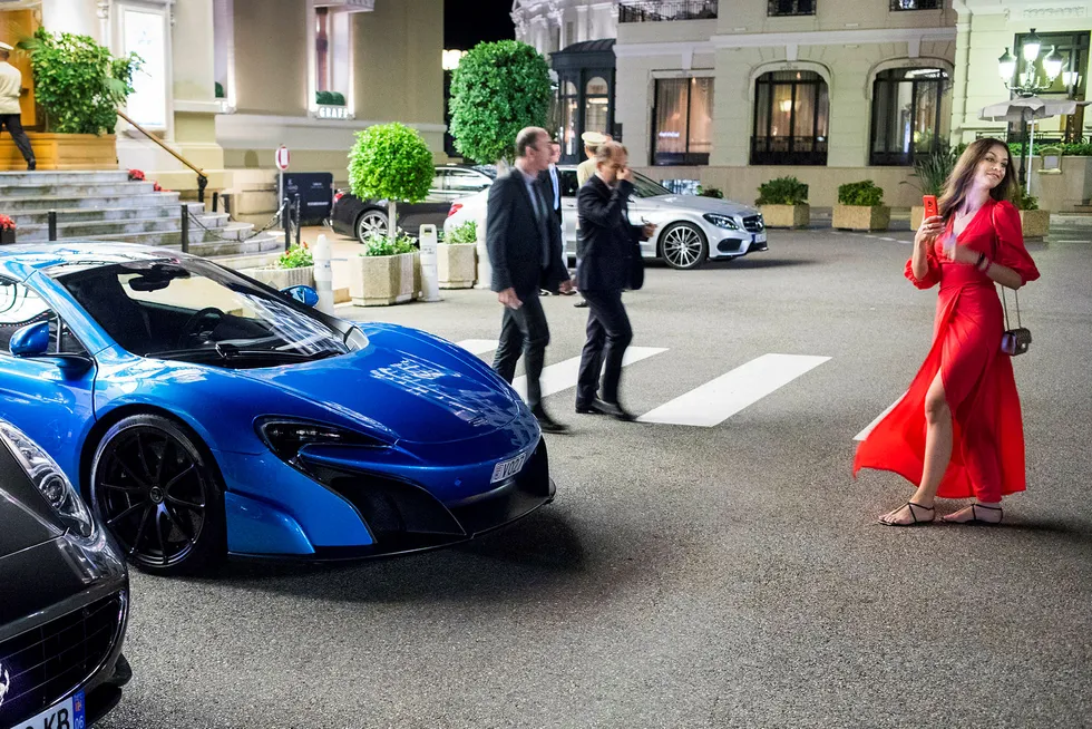 Fotoshoot. En svart Ferrari, en blå McLaren og en turist i rød kjole gjør seg klar til fotografering foran Casino de Monte-Carlo.