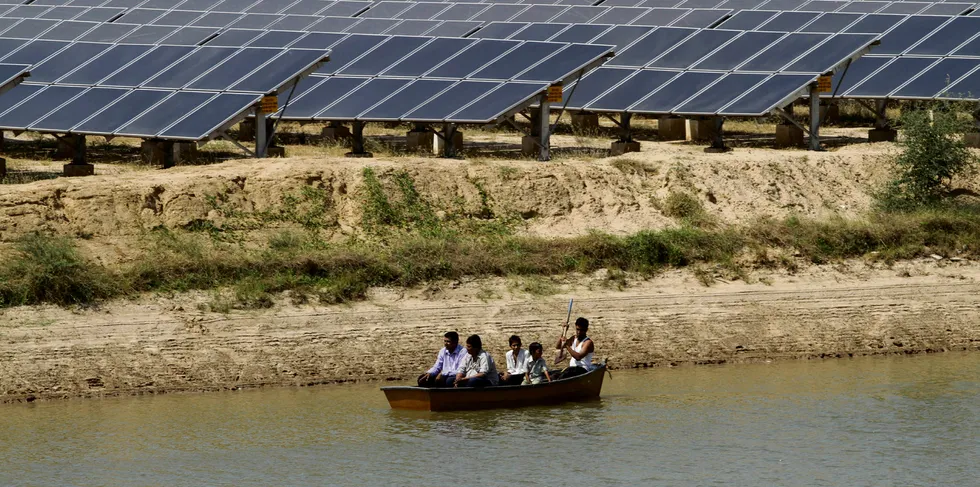 A boat passes by panels at a newly inaugurated solar energy farm at Gunthawada in Gujarat state.