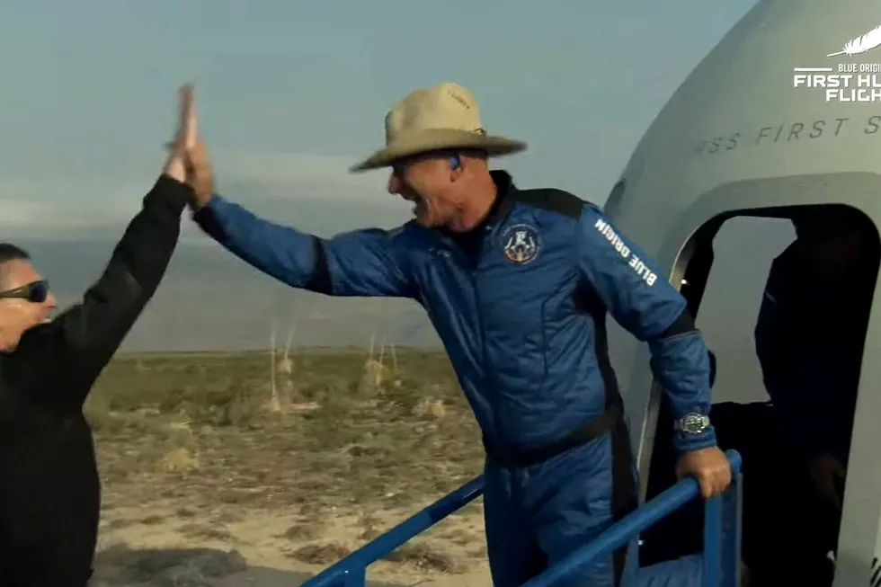 Jeff Bezos stiger ut av romkapselen og blir møtt med en high-five etter den vellykkede oppskytningen.