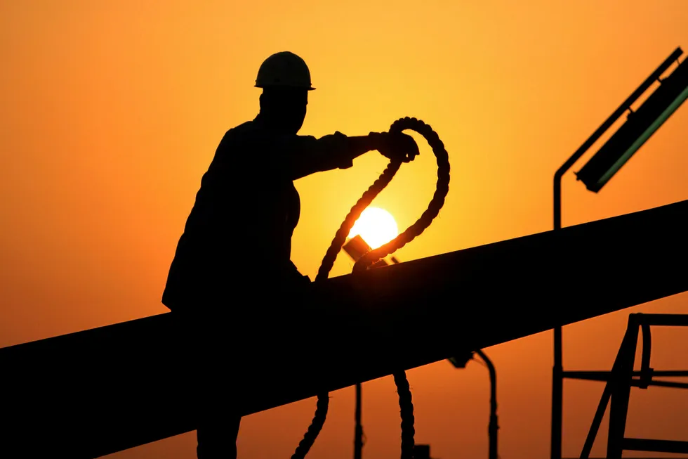 An oilfield worker ties pipes to be raised on an oil rig as the sun sets in the Persian Gulf desert oil field of Sakhir, Bahrain
