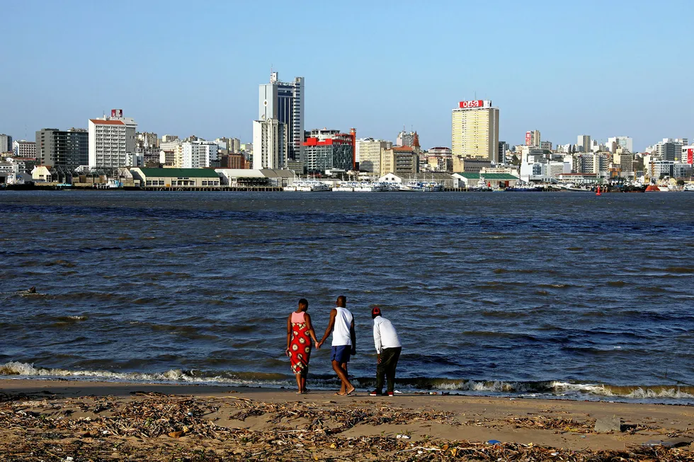 On the horizon: locals take a walk along a beach with the Maputo skyline in the background