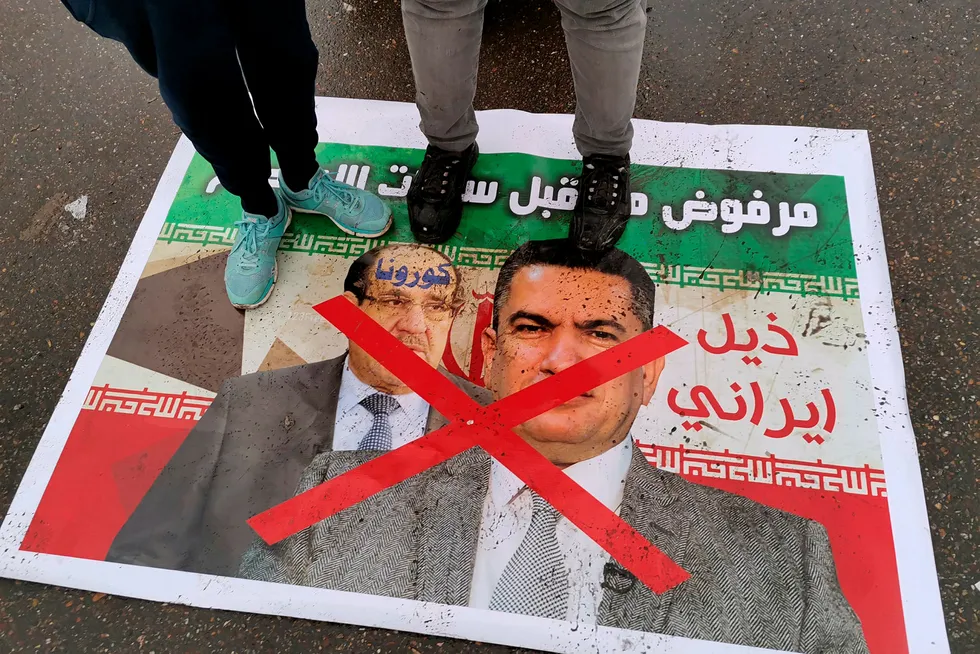 Tough days ahead: anti-government protesters stand on a defaced poster with pictures of former Iraqi Prime Minister Nouri al Maliki, left, and Iraq's Prime Minister-designate Adnan al Zurfi