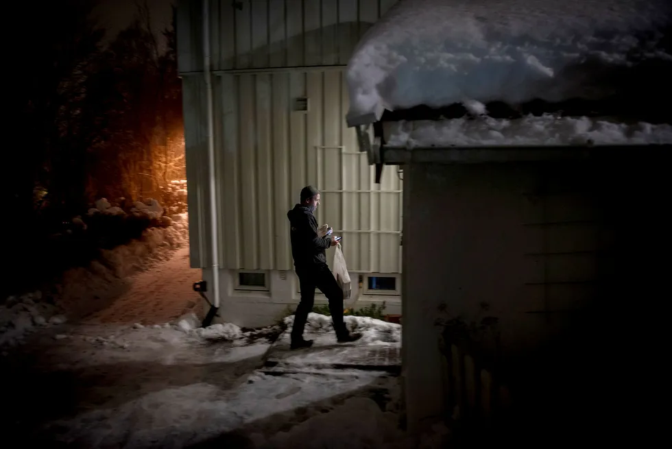 Rune Johansen fra budtjenesten Helthjem henger en pose med ferske brødvarer på døren til en kunde. To aviser legges på dørmatta. Foto: Gorm K. Gaare