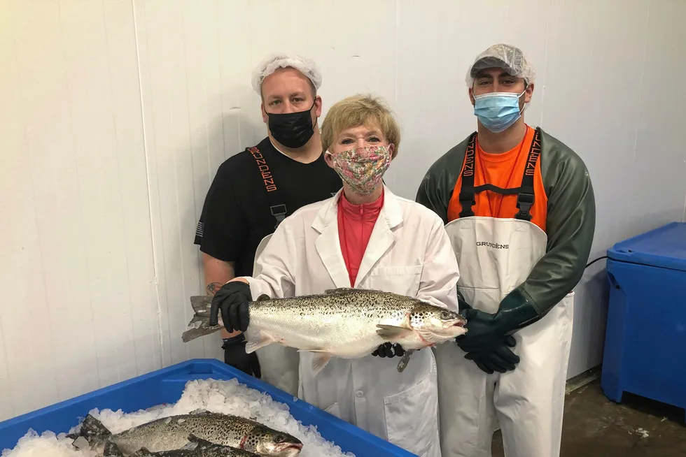 AquaBounty Processing Associates Skyler Miller (left) and Jacob Clawson (right), with CEO Sylvia Wulf (center) holding the first commercially harvested genetically modified farmed salmon in the United States. The company is decreasing its GM salmon production in Canada.