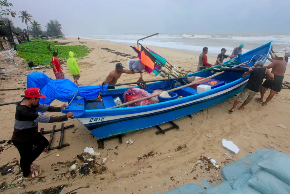 Moving a vessel: men push a boat on a beach in Songkhla, Thailand
