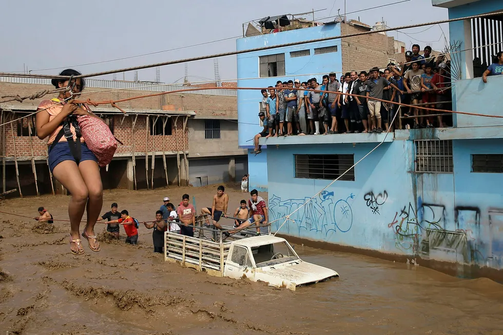 En kvinne blir heist i sikkerhet over en gate som er forvandlet til en elv i Lima i Peru. Foto: Martin Mejia / AP / NTB Scanpix