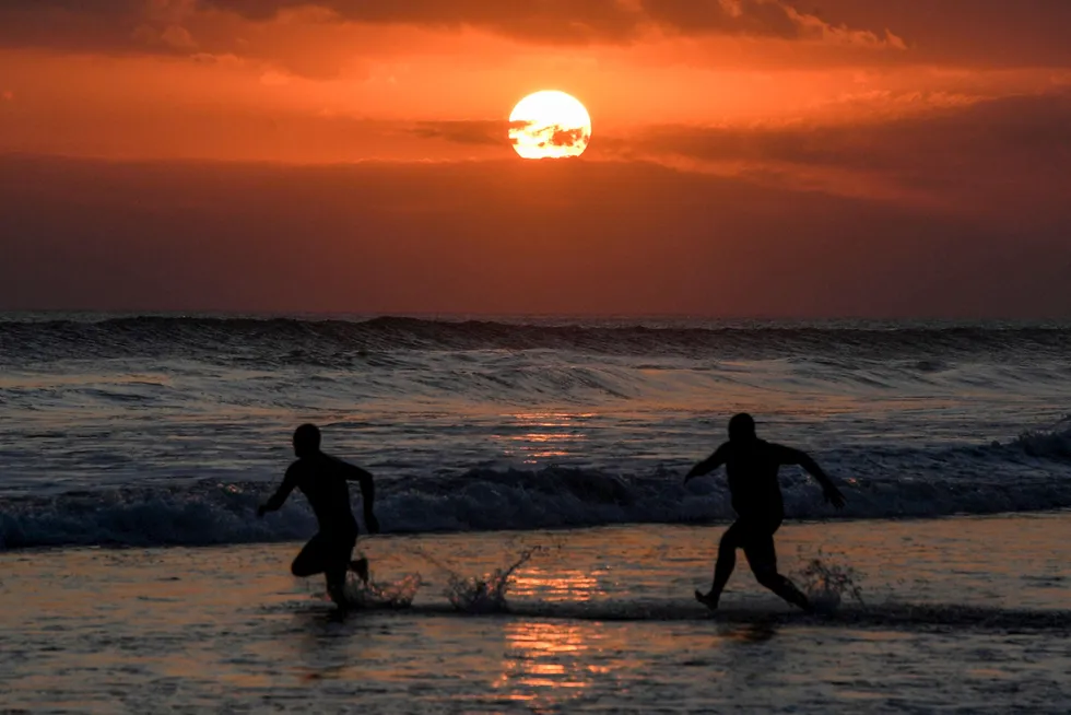 Sunset: people run into the sea on Mesari beach in Seminyak, Indonesia.