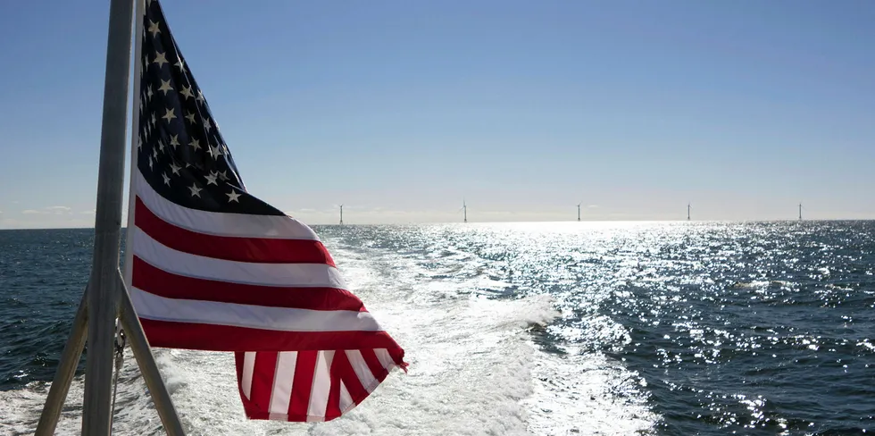 A US flag flies off the back of a boat with the five turbines of America's first offshore wind farm, the 30MW Block Island project, on the horizon.