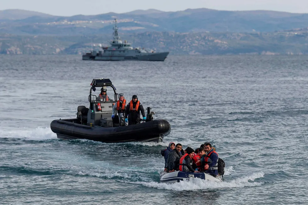 Flyktninger i båt på vei inn til Hellas fra Tyrkia med kystvakt i bakgrunnen.
