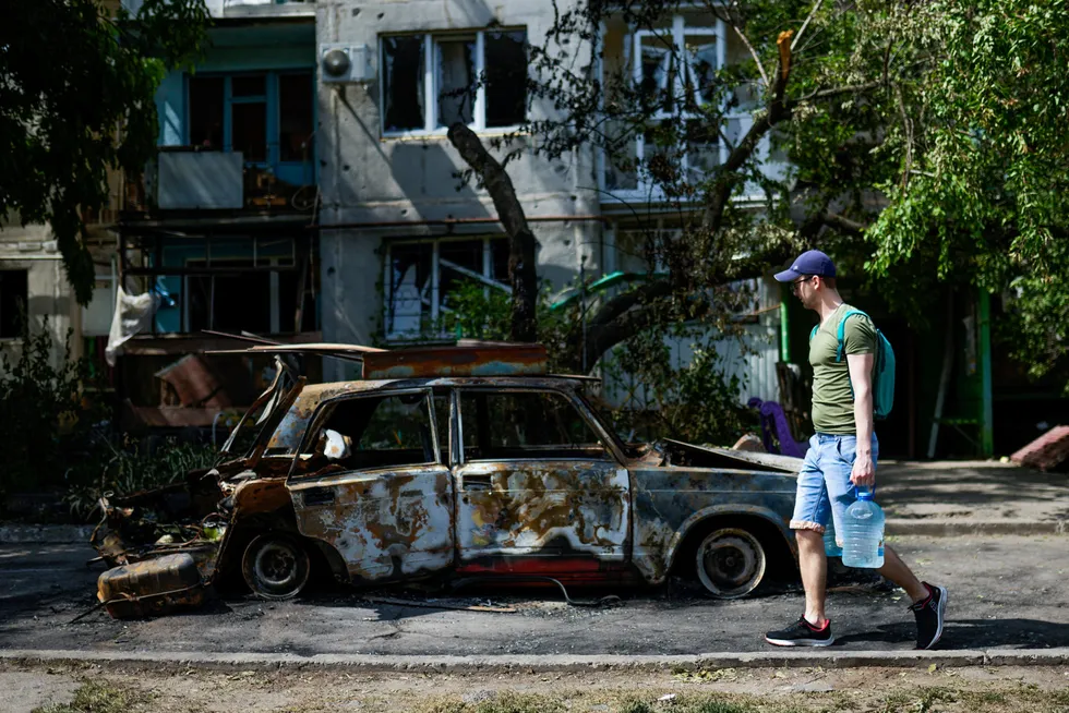 En mann går med en vannbeholder forbi restene av en bil som ble ødelagt i et rakettangrep i Slavjansk 31. mai.