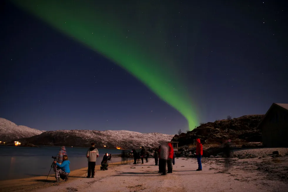 Et titall turister fotograferer og opplever nordlys på stranden til Tromsø Friluftssenter i Risvika på Kvaløya utenfor Tromsø.
