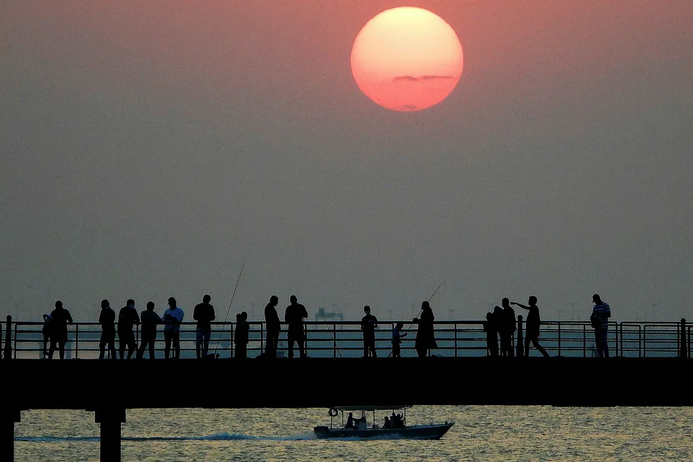 Jurassic plans: people walk along a boardwalk that stretches into the sea as the sun sets over Kuwait City