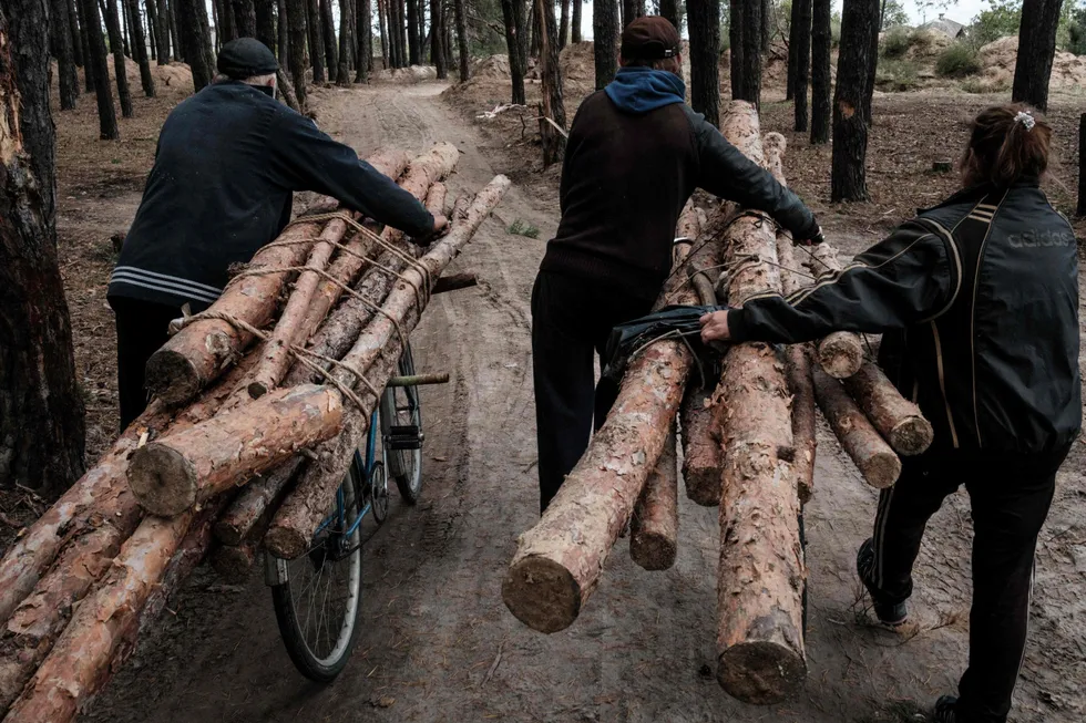 TOPSHOT - Residents carry logs from the trenches used during Russia's occupation near the mass grave to make firewoods before winter, in Izyum, Kharkiv region, on September 25, 2022, amid the Russian invasion of Ukraine. (Photo by Yasuyoshi CHIBA / AFP)