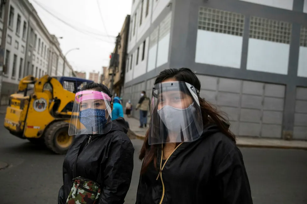 To kvinner med munnbind og visir, som har vært påbudt på offentlig transport i bykjernen i Perus hovedstad Lima. Landets økonomi har gått inn i resesjon som følge av koronapandemien.