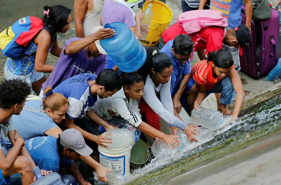 Folk forsøker desperat å samle opp vann fra en lekk vannledning ved elven Guaire i Venezuelas hovedstad Caracas.
