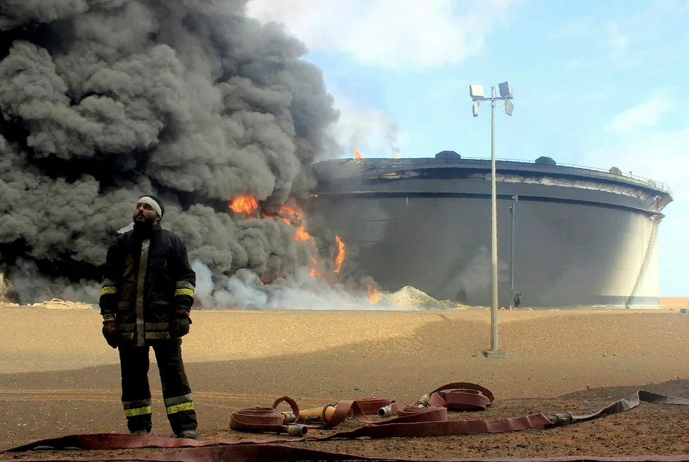 En libysk brannmann foran en oljelagerfasilitet i brann fra den oljerike Ras Lanuf-regionen i fjor. Det er dette området ulike militsgrupper nå kjemper over i Libya. Foto: Afp/NTB Scanpix