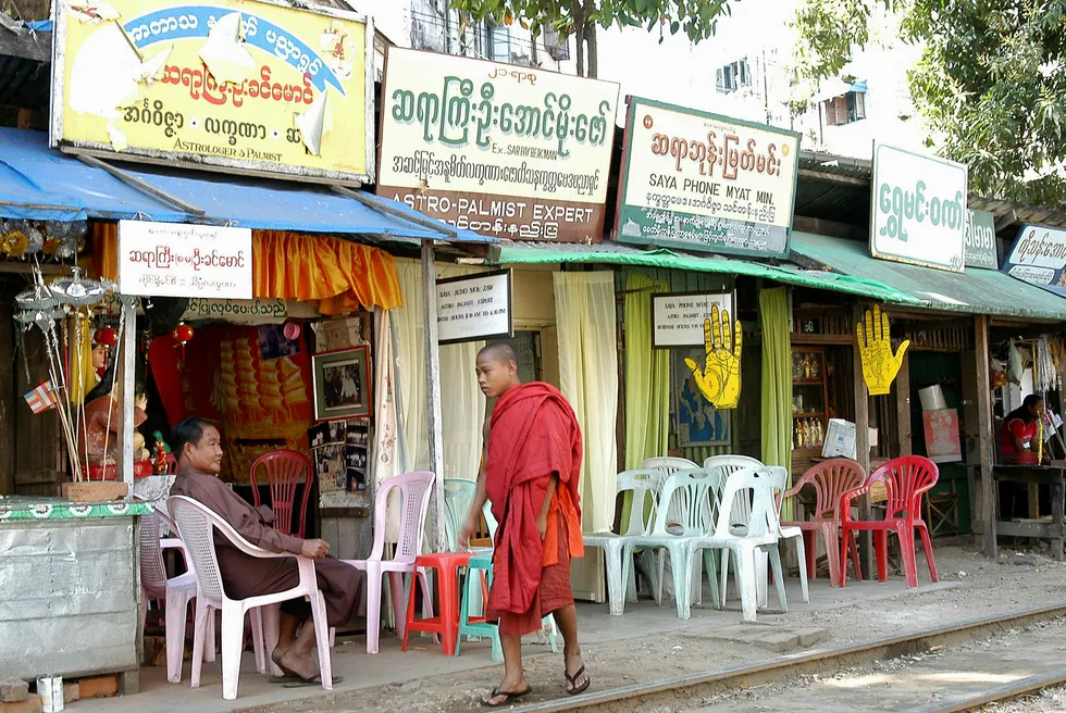 Before lockdown: a Myanmar fortune teller relaxes in front of his consulting room as a Buddhist monk passes by in the former capital Yangon