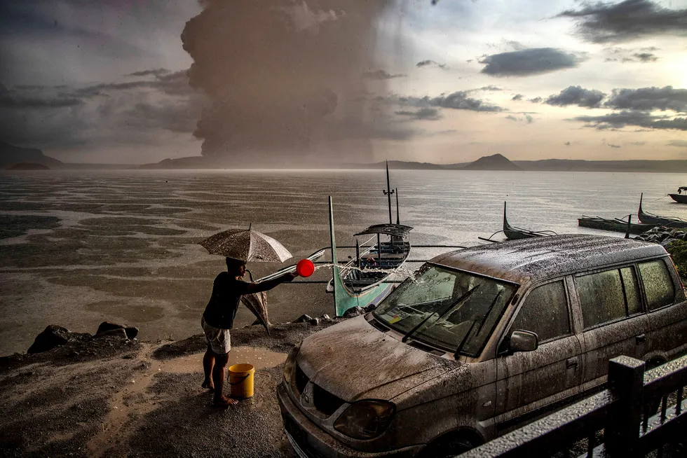 En mann vasker bilen for aske og regnvann etter utbruddet i Taal-vulkanen på Filippinene. Vulkanen ligger på en øy i en innsjø 66 kilometer sør for hovedstaden Manila, og søndag sendte den damp og aske en kilometer opp i luften.