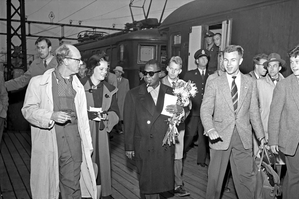 Verdensstjernen Louis Armstrong ankommer Oslo Østbanestasjon i oktober 1955 og blir mottatt med blomsterbukett av jazzmusikeren Gerhard Aspheim (bak til venstre) og Aftenpostens jazzjournalist Stein Kagge (til høyre) Foto: NTB Scanpix Foto: NTB scanpix