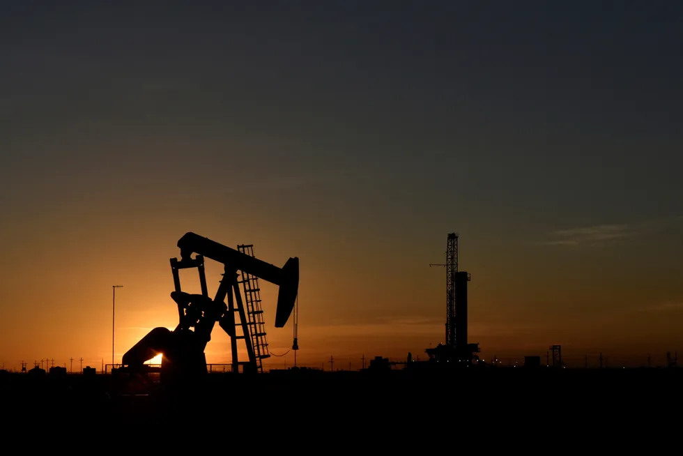 Consolidation: A pump jack operates in front of a drilling rig at sunset in an oilfield in Midland, Texas US.
