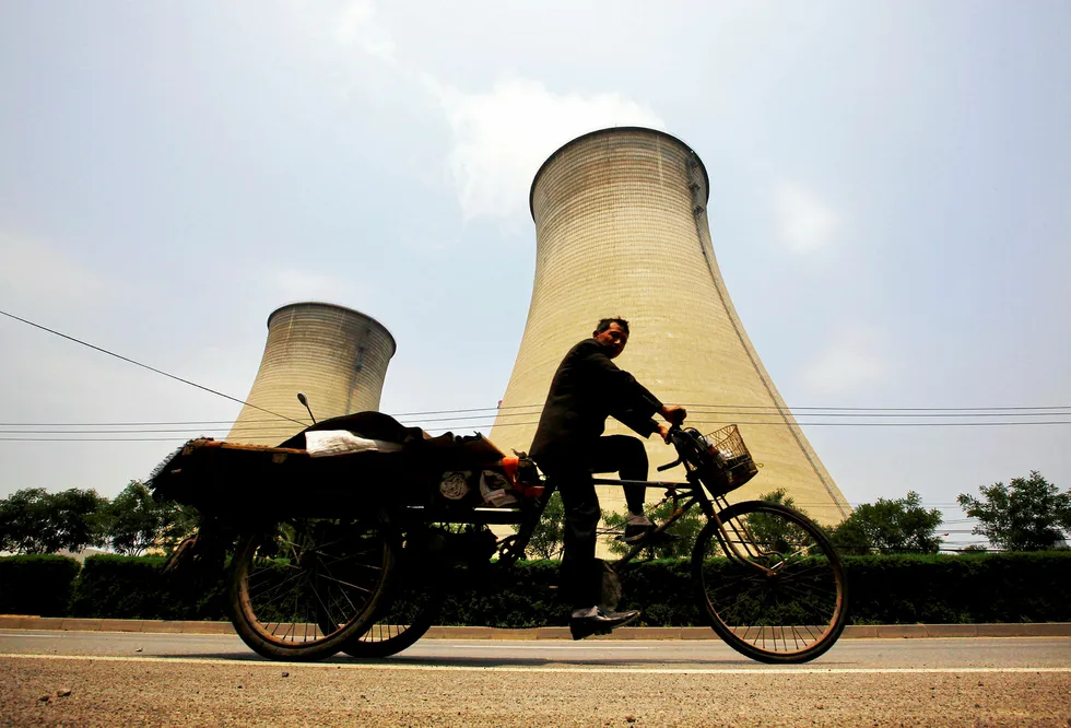 All change: a man rides his tricycle past the cooling tower and chimneys of a coal-burning power station in Beijing