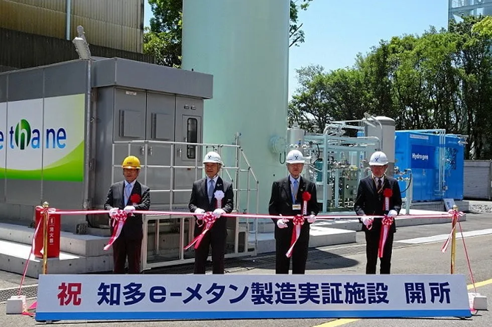 The ribbon-cutting ceremony for the project in Chita, Aichi prefecture. The blue structure on the right is the electrolyser, and the dark grey structure on the left (labelled 'e-methane' in English) contains the Sabatier equipment. The sign at the front reads: 'Congratulations [in red] Chita e-methane production demonstration facility opened'