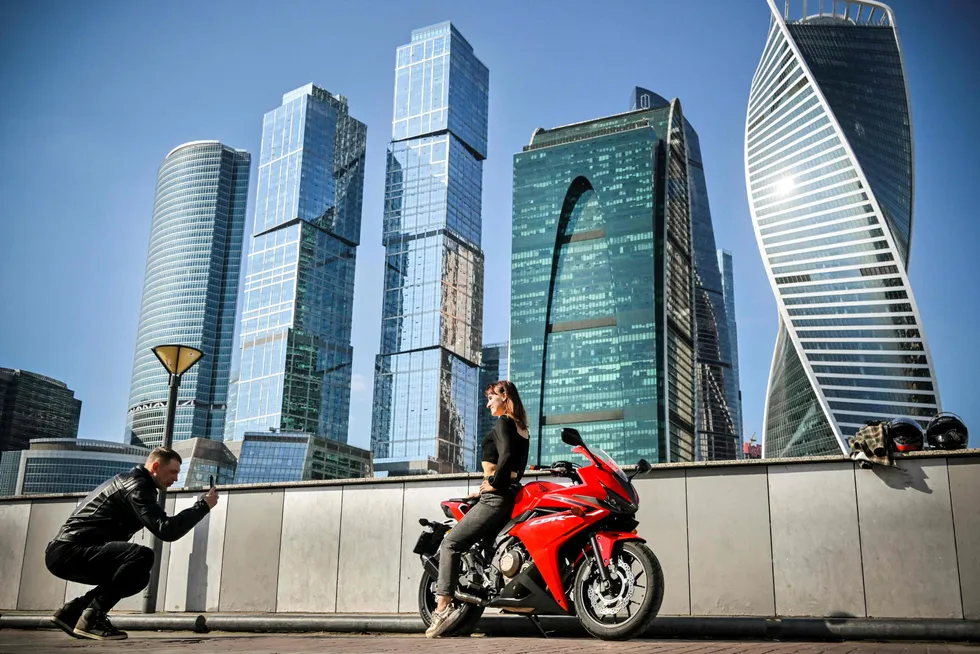 En mann fotograferer en kvinne poserende på en motorsykkel. I bakgrunnen Moskvas internasjonale business senter, Moskva City.