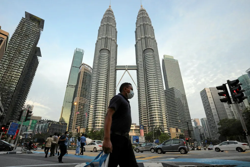 Limbayong chase: a man wearing a protective mask crosses a street in front of Petronas Twin Towers, Kuala Lumpur