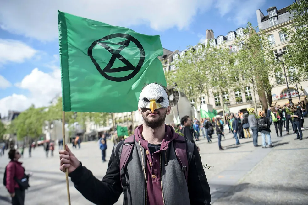 En klimaaktivist fra Extinction Rebellion under en demonstrasjon i Paris holder organisasjonens flagg med et symbol som viser et timeglass inne i en sirkel.