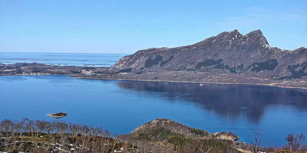 En fin vårdag i Meløy kommune på Helgeland. Midt på bildet ligger ser vi et oppdrettsanlegg.