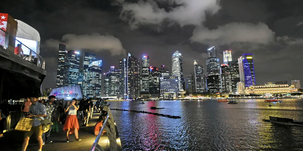 People walking on a promenade in front of the skyline of the Singapore financial business district at night.
