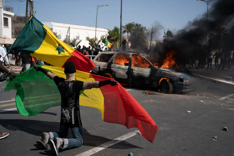 Fired up: a young demonstrator holds a Senegalese flag as he kneels in front of a burning car during protests in Dakar against the arrest of opposition leader and former presidential candidate Ousmane Sonko