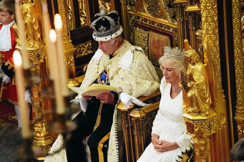 King Charles III, wearing the Imperial State Crown and the Robe of State, reads the King's Speech, beside Queen Camilla.