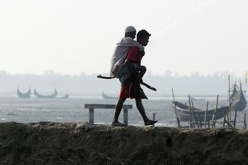Humanitarian crisis: a Rohingya refugee carries his father on his back as they arrive at a port after crossing the Bangladesh-Myanmar border