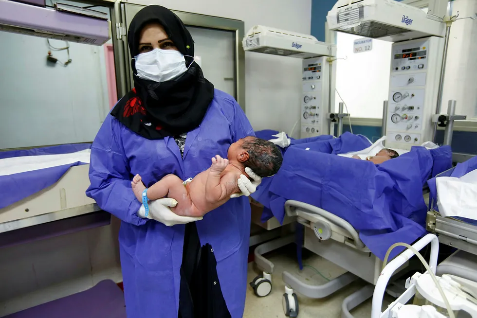 En sykepleier beskyttet mot koronavirus tar seg av en nyfødt på et sykehus i Najaf, Irak.