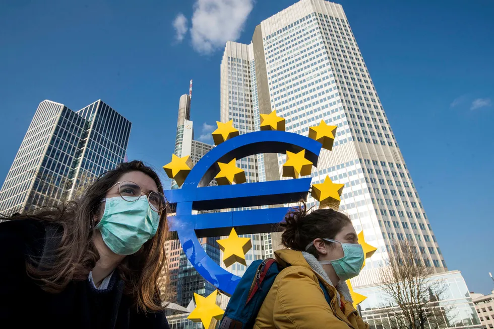 I bunnen handler det om selve eurokonstruksjonen, som aldri har vært laget for å tåle økonomisk stormvær. Her sykler to studenter med ansiktsmasker forbi en euroskulptur i Frankfurt i Tyskland.