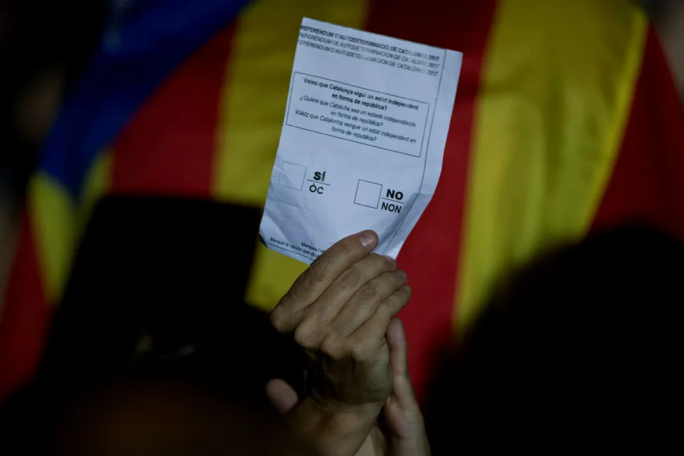 En kvinne holder en uoffisiell valgslipp ved siden av et uavhengighetsflagg under et arrangement som fremmer løsrivelse av regionen Catalonia fra resten av Spania. Foto: Emilio Morenatti / AP / NTB Scanpix