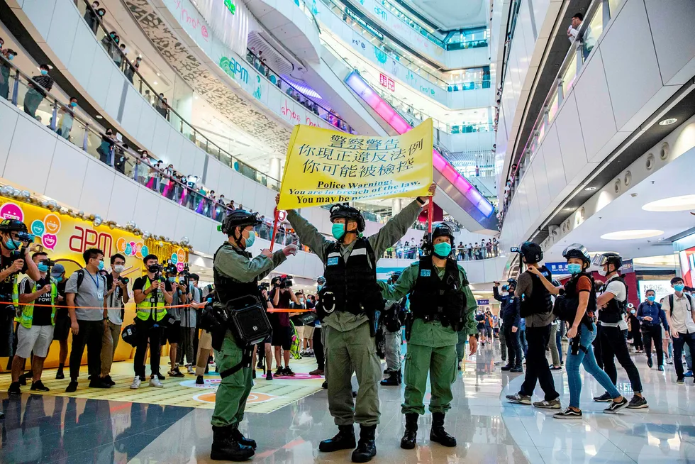 Opprørspoliti inne på et kjøpesenter i Hong Kong mandag denne uken holder opp en plakat som advarer demonstranter om at de kan bli straffeforfulgt.
