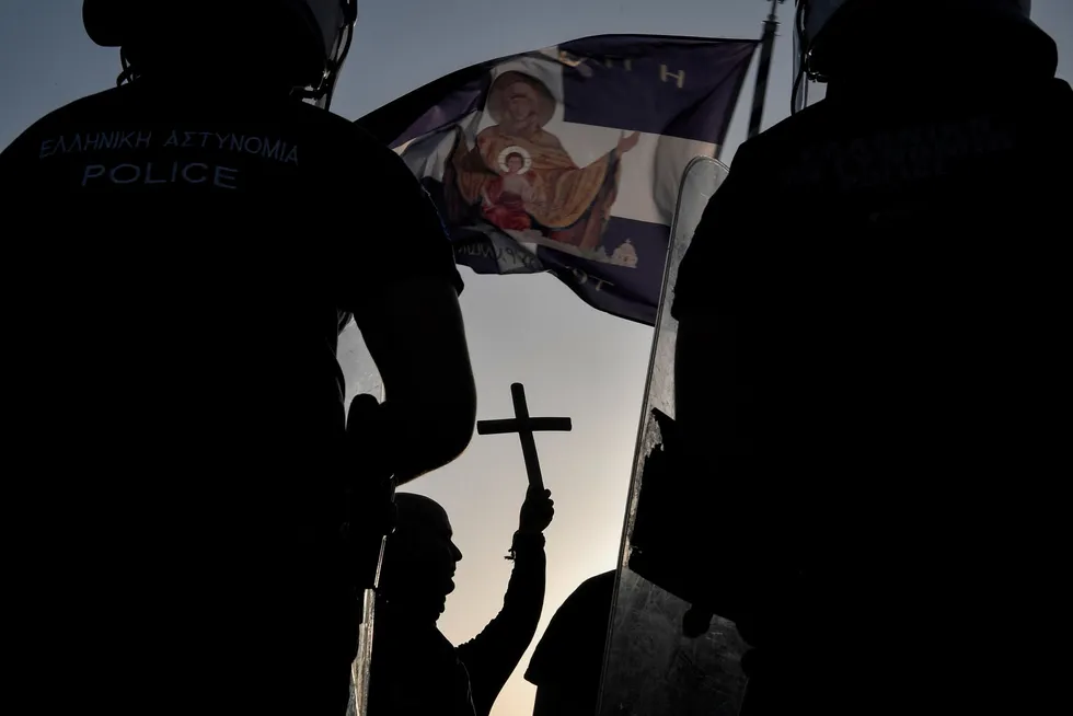 Vaksinemotstander løfter korset foran politisperring under demonstrasjon i Aten 28. juli.